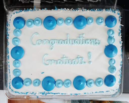 A white sheet cake with the text "Congraduations Gratuate!" written on it in blue icing