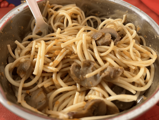 A close up of spaghetti and mushrooms. There's a small amount of orange sauce. A white plastic fork can be seen.