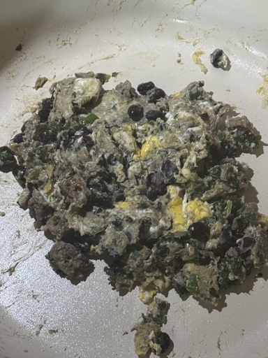  a plate of eggs with black beans that looks like an infected goblin shat it out