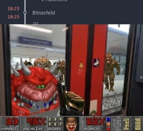​Ein Meme, das die Benutzeroberfläche des Ego-Shooter-Spiels "Doom" (1993) über ein Foto legt, das aus dem Inneren eines Zuges aufgenommen wurde. Der untere Teil des Bildes zeigt das klassische "Doom"-HUD. Der Blick durch die Zugtüren zeigt einen Bahnsteig, auf dem statt Menschen mehrere Dämonen aus dem Spiel stehen, darunter Imps und ein Cacodemon. Oben im Bild ist eine digitale Haltestellenanzeige eines öffentlichen Verkehrsmittels zu sehen, die den nächsten Halt anzeigt: "18:25 Bitterfeld".